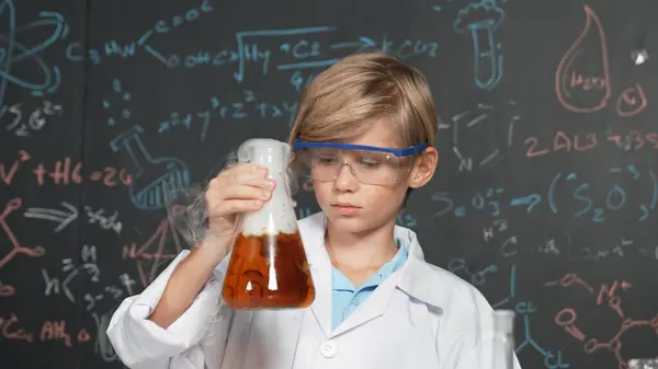 Smart boy inspect mixed chemical liquid in laboratory beakers while holding and looking carefully. Caucasian child focus on doing an experiment in chemistry lesson or STEM science class. Erudition.