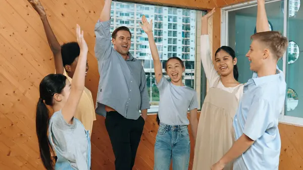 Smart teacher and diverse student standing while putting hand in the air to celebrate successful project.. Skilled instructor with highschool children with mixed races in casual outfit . Edification.
