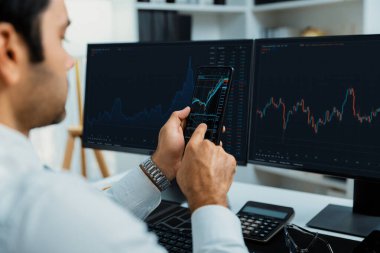 Akıllı telefondan akıllı telefon arayan tüccar işadamı, bilgisayardaki dinamik borsa yatırım ekranını analiz ediyor ve modern merkez ofisteki en kârlı finansal teknoloji pazarına yatırım yapıyor. Tahmin et..