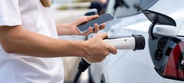 EV 'yi şarj etmek için elektrikli araca EV şarj prizi tak, akıllı telefon EV uygulamasında pil durumu görüntüsü. Ulaşım için alternatif temiz ve sürdürülebilir enerji. Kalıcı