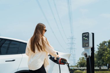 Genç kadın elektrik şebekesine bağlı elektrik şebekesine bağlı EV araba aküsünü elektrik endüstrisi olarak şarj ediyor. Çevre dostu araç kullanımı için. Yararlı