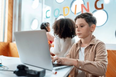 Sınıfta oturan ve diğer çocuklar dışarıyı izlerken bilgisayarla uzaktan kumanda mühendisliğini öğrenen öğrenci. Devre teli, anakart ve defter dağınık bir şekilde masaya konmuş. Etkinlik.