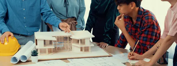 Architect team analysis and brainstorming about house construction at meeting table with house model, blueprint and architectural equipment scatter around. Creative design and teamwork. Burgeoning.