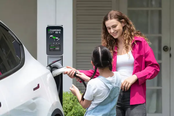 幸せな小さな少女は 母親がEv充電ステーションから電気自動車を充電するのを助けるため 環境にやさしいエネルギーの持続可能性について学びます Evカーとモダンなファミリーコンセプト シンクロノス — ストック写真
