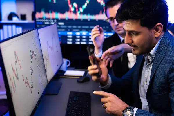 stock image Two stock exchange traders researching data on smartphone and laptop screen server of dynamic digital currency. Investors analyzing market stock at decorative neon blue-light of workplace. Sellable.