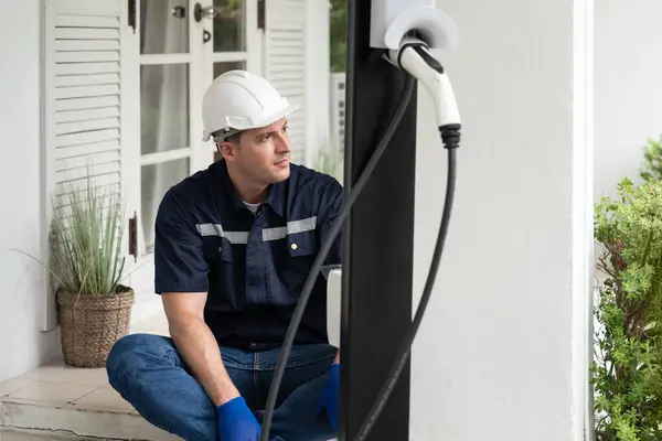 Qualified technician install home EV charging station, providing maintenance service for electric vehicles battery charging platform at home. EV car technology for residential utilization. Synchronos