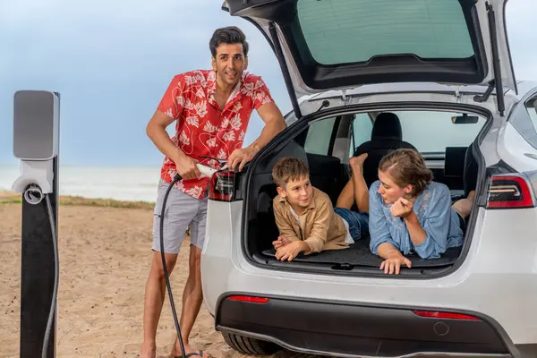 電気自動車でビーチで旅行する家族旅行 素敵な家族はトランクに座って 緑と持続可能なエネルギーでEvカーバッテリーを充電します 家族旅行と環境に優しい車 パーペチュアル — ストック写真