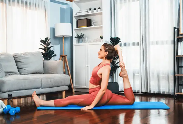 在家里锻炼垫子时 穿着运动服的灵活而敏捷的女人在冥想的姿势下做瑜伽 安详祥和的家庭瑜伽生活方式 — 图库照片