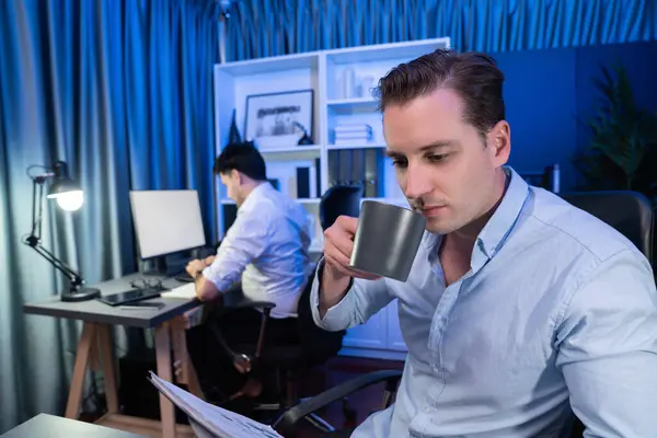 ビジネスパートナーは 現代のオフィスで夜間にドキュメントシート作業に焦点を当てたコーヒーを飲む ブルーネオンデコレーションルームのクリエイティブプロジェクトでコンピュータを分析 販売可能 — ストック写真