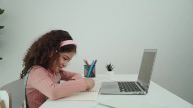 Kulaklık takan ve ev ödevi yapan bir kızın yan görüntüsü. Programlama sistemini araştırırken ve mühendislik komut yazarken defterde yazan mutlu çekici kız öğrenci. Pedagoji.