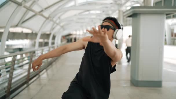 聪明英俊的舞蹈家一边手舞足蹈一边跳嘻哈音乐 专业的亚洲嬉皮士头戴耳机 带着模糊的背景在走廊上行走 2024年户外运动 神气活现 — 图库视频影像