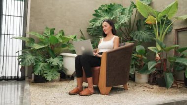 Modern genç kadın telefonda konuşuyor, uzaktan çalışıyor ya da tropik bitkilerle birlikte minimalist bir mimari beton stil yaz egzotik bitki yetiştirme bahçesinde yalnız başına dinleniyor. Blithe