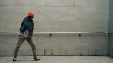 Asyalı akıllı hipster, kulaklık ve şık kıyafetler giyip hip hop şarkıları dinlerken gri arka planlı enerjik break dans gösterisi yapıyor. Açık hava sporu 2024. Hip hop hareketi. Yumuşak bir şekilde..