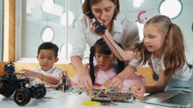 Genç, beyaz bir öğretmen çeşitli öğrencilere elektronik yönetim kurulunu öğretiyor. Çok kültürlü çocuklar dijital elektrikli aletleri ve ana kartı çip ve kablolar kullanarak tamir etmeyi öğrenirler. Etkinlik.