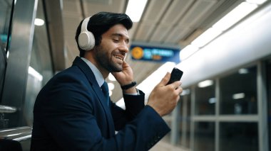 Tren istasyonunda geçmişi bulanık bir şekilde beklerken kulaklıkla müzik dinleyen zeki bir iş adamı. Yetenekli proje yöneticisi cep telefonu tutarken dinlenme sesi dinlemeyi sever. Sevinçli..