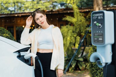 Genç kadın ve sürdürülebilir kentsel yol, bahar bahçesi, yeşil şehir sürdürülebilirliği ve çevre dostu EV arabadaki açık kafede çalışan EV elektrikli araba. Yararlı