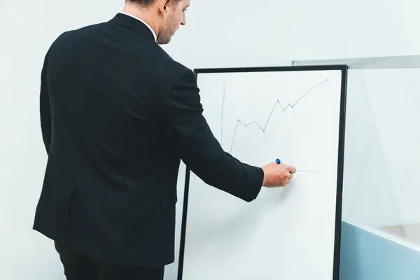 Closeup of smart male leader drawing increasing graph at business meeting room while standing at whiteboard at business meeting. Caucasian businessman present business sales statistic. Ornamented.