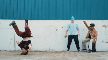 Genç Asyalı dansçı hip hop tarzında dans ediyor ve çok kültürlü arkadaşları duvarın arkasında tezahürat yapıyor. Çekici yakışıklı adam mavi arka planda kollarını uzatıyor. Açık hava sporu 2024 hiphop..