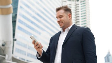 Kafkasyalı iş adamı şehir merkezinde dururken cep telefonlarını kontrol ediyor ve pazarlama ekibinden satış raporlarını inceliyor. Yetenekli bir yönetici cep telefonu üzerinde çalışıyor ve veri analizine bakıyor. Urbane.