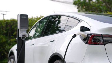 Doğal yeşil şehir parkındaki otoparkta EV elektrikli araba şarj pili. Sürdürülebilir ve çevre dostu şehir yolculuğu için yenilenebilir otomobil için alternatif temiz enerji teknolojisi. Eşzamanlama