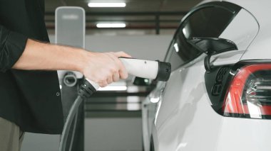 Genç adam EV elektrikli arabasıyla şehir merkezindeki alışveriş merkezinin otoparkına gidiyor şehir merkezindeki sürdürülebilirlik yaşam tarzını yeşil, temiz, yeniden şarj edilebilir elektrikli araç iç organlarıyla şarj ediyor.