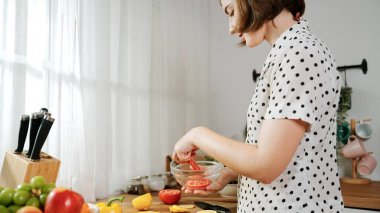 Kafkaseli anne kahvaltıda sebze pişirirken mutlu anne de modern mutfakta salata için taze malzemeler hazırlıyor. Hizmetçi sağlıklı yemek pişiriyor. Dikkat konsepti. Pedagoji.
