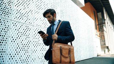 Akıllı yönetici cep telefonuna bakıyor ve takım elbise giyerken sokakta yürüyor. Yetenekli yatırımcı cep telefonuyla satışları kontrol ediyor ya da elinde kahve fincanı tutarken çalışıyor. Beyaz arka plan. Sevinçli..