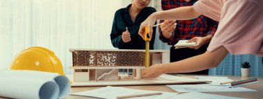 Akıllı mimar mühendis ve iç mimar birlikte çalışıyor ve ev modelini ölçmek için plan ve mimari ekipmanlarla toplantı masasında cetvel kullanıyor. Takım çalışması konsepti. Filizlenen.