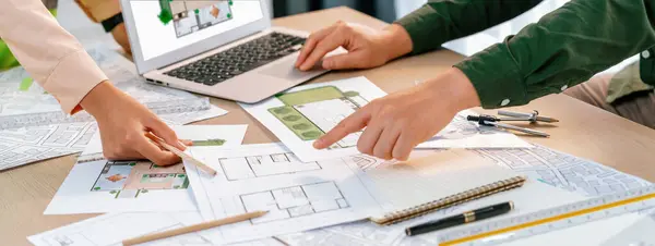 Professional architect shows mistake structure in blueprint while analysis and comparison with picture in laptop on table with blueprint and architectural equipment. Cropped image. Delineation.