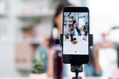 Seçici odaklı akıllı telefon ve gülümseyen genç, güzel Asyalı karışık çilek ve kiraz suyu detoksu değerlendirmesi sosyal medyada sağlıklı ürün tanıtımı sunuyor. Taktik.