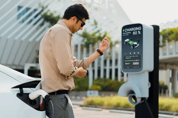 年轻人把电动汽车充电器从城市商业停车场的充电站充电给电动汽车充电 可再生能源电动汽车用于可持续环境友好型城市旅行 — 图库照片