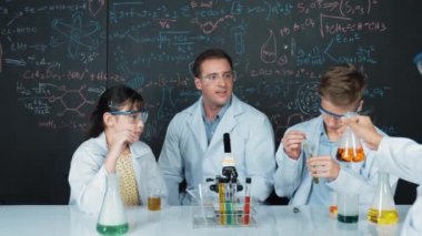 Zeki kız, çeşitli öğrenciler STEM fen dersinde deney yaparken renkli sıvıyı inceliyor. Bir grup liseli çocuk tahtada dururken laboratuvarda çalışıyor. Yaratıcı. Öğretim