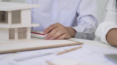 Profesyonel erkek mühendis ev modelini cetvel kullanarak ölçerken güzel bir kooperatif iş arkadaşı verileri analiz etmek için dizüstü bilgisayar kullanarak birlikte çalışıyor. Yaratıcı tasarım ve takım çalışması. - Yakın çekim. Tertemiz..