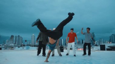 Profesyonel hippi hareketsiz poz verirken aynı zamanda şehir manzaralı çatıdaki müziğe ayak basıyor. Break dansçı, hip-hop dansçıları grubuyla birlikte sokak dansı yapıyor. Açık hava sporu 2024 hiphop..
