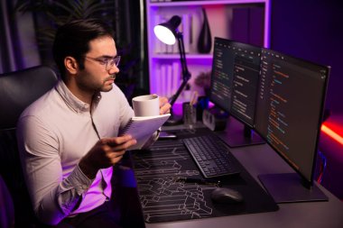 Akıllı bilişim geliştiricisi, bilgisayar ekranındaki yazılım geliştirme kodlaması üzerine kahveyle birlikte çalışıyor, en yeni uygulama projesi programı ile birlikte neon ışıklı siber ofiste çevrimiçi web sitesi verilerini güncelliyor. Tahmin et..