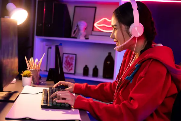 stock image Host channel of smiling beautiful Asian girl streamer playing online game wearing headphone talking with viewers media online recording phone. Esport skilled team players in neon blue room. Stratagem.