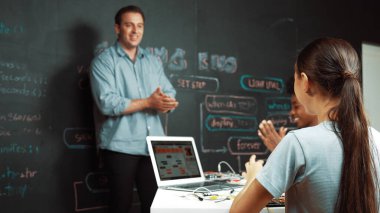 Kafkas öğretmeni alkışlayarak öğrencileri kodlamayı veya programlamayı teşvik etmek için alkışlıyor. Çeşitli öğrenciler STEM sınıfına katılırken başarılı bir projeyi kutlamak için el çırpıyorlar. Öğretim.