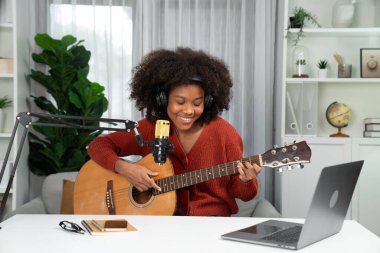 Genç Afrikalı Amerikalı müzisyenin sunucu kanalı gitar çalıyor, şarkı söylüyor, stüdyoda dizüstü bilgisayardan yayın yapıyor. Kulaklık dekorasyonu ve mikrofon kaydı. Tatlandırıcı.