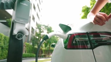 Yavaş çekim çift yazın yeşil sürdürülebilir şehir açık bahçesinde elektrikli araba şarj ile seyahat elektrikli aracın temiz yeniden şarj edilebilir enerjisi için kentsel sürdürülebilirlik yaşam tarzı olarak