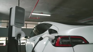 Şehir merkezindeki kapalı otoparkta yavaş çekimde EV elektrikli araba şarj oluyor. Şehir merkezinde sürdürülebilirlik yeşili, yeniden şarj edilebilir elektrikli araç iç organları.