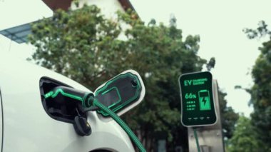 Doğal yeşil araba parkındaki ekolojik temiz enerji şarj istasyonundan gelen fütürist akıllı EV şarj aletinin şarj ettiği elektrikli araba. Alternatif enerji kullanan gelecekçi çevre dostu elektrikli araba. İnceleyin