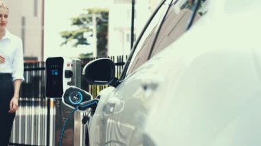 Alışveriş çantalı bir iş kadını, otopark veya alışveriş merkezindeki akıllı dijital batarya durum hologramını şarj ediyor. Gelecekçi yaşam tarzı ve çevre dostu araba. İnceleyin