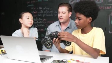 Afrikalı çocuk araba modelini dizüstü bilgisayar ve kabloyla incelerken öğretmen de karatahtadaki robotik yapıyı şifreli ya da STEM sınıfında hızlı bir şekilde açıklıyor. Eğitim. Öğretim