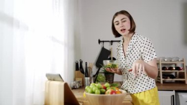 Mutlu genç anne mutfakta dururken salata kasesine sebze koydu. Çekici beyaz bir kadın yemek pişirmekten ve sabah taze organik yemek yapmaktan ya da ev yemeği yapmaktan zevk alır. Pedagoji.