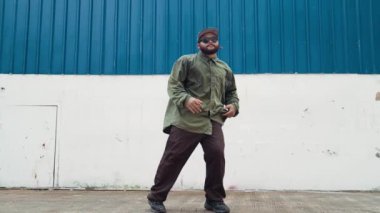 Sokak ortasında mavi duvarlı hippi dansçı ayak basamağı. Asyalı break dansçı kollarını açarken sokak dansı yapıyor. Hip hop koreografı enerjik bir dans sergiliyor. Açık hava sporu 2024 hiphop..