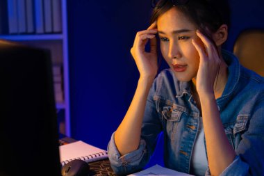 Stresli, genç, güzel Asyalı yaratıcı proje yaratıcısı sosyal medyayı araştırmak için bilgisayara bakıyor ve geceleri daha çok neon modern ofisin planlama kanalı stratejisine ulaşılıyor. Taktik.