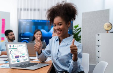 Bir grup ofis çalışanı ile birlikte arka planda ekranda gösterim paneliyle buluşan mutlu Afrikalı genç bir iş kadını portresi. Takım toplantısında kendine güveni tam bir ofis hanımı. Uyum