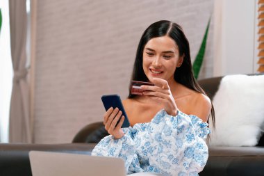 Genç bir kadın kredi kartıyla ödemek için dijital cüzdan ve internet üzerinden ödeme uygulaması kullanıyor. Mobil internet üzerinden alışveriş ve modern alımlar. Blithe