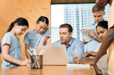 Ders sırasında öğretmenler oturur ve dizüstü bilgisayar kullanır. Ayakta duran ve birlikte not aldıkları için iki gruba ayrılan öğrenciler de dersten bahsediyorlar. Masaya kalem kutusu koyun. Öğretim.