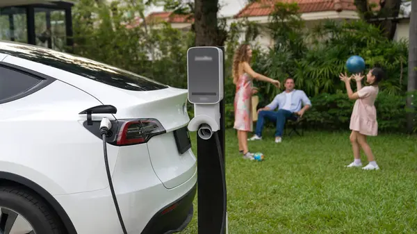 幸せで遊び心のある家族が一緒に遊ぶ背景にある家庭用充電ステーションからの電気自動車の充電 より良い未来のシンクロノスのための代替エネルギーと持続可能なエネルギーを使用したEv車 — ストック写真